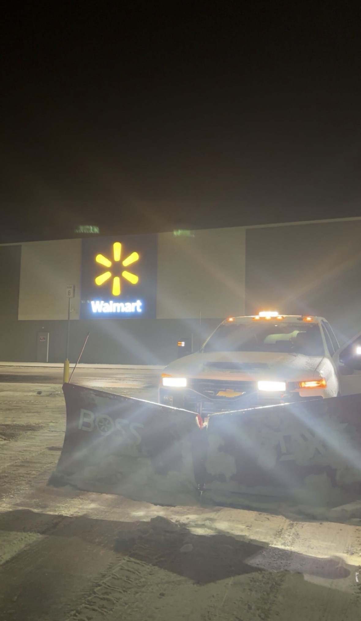 Swift plow truck clearing a retail store parking lot at night