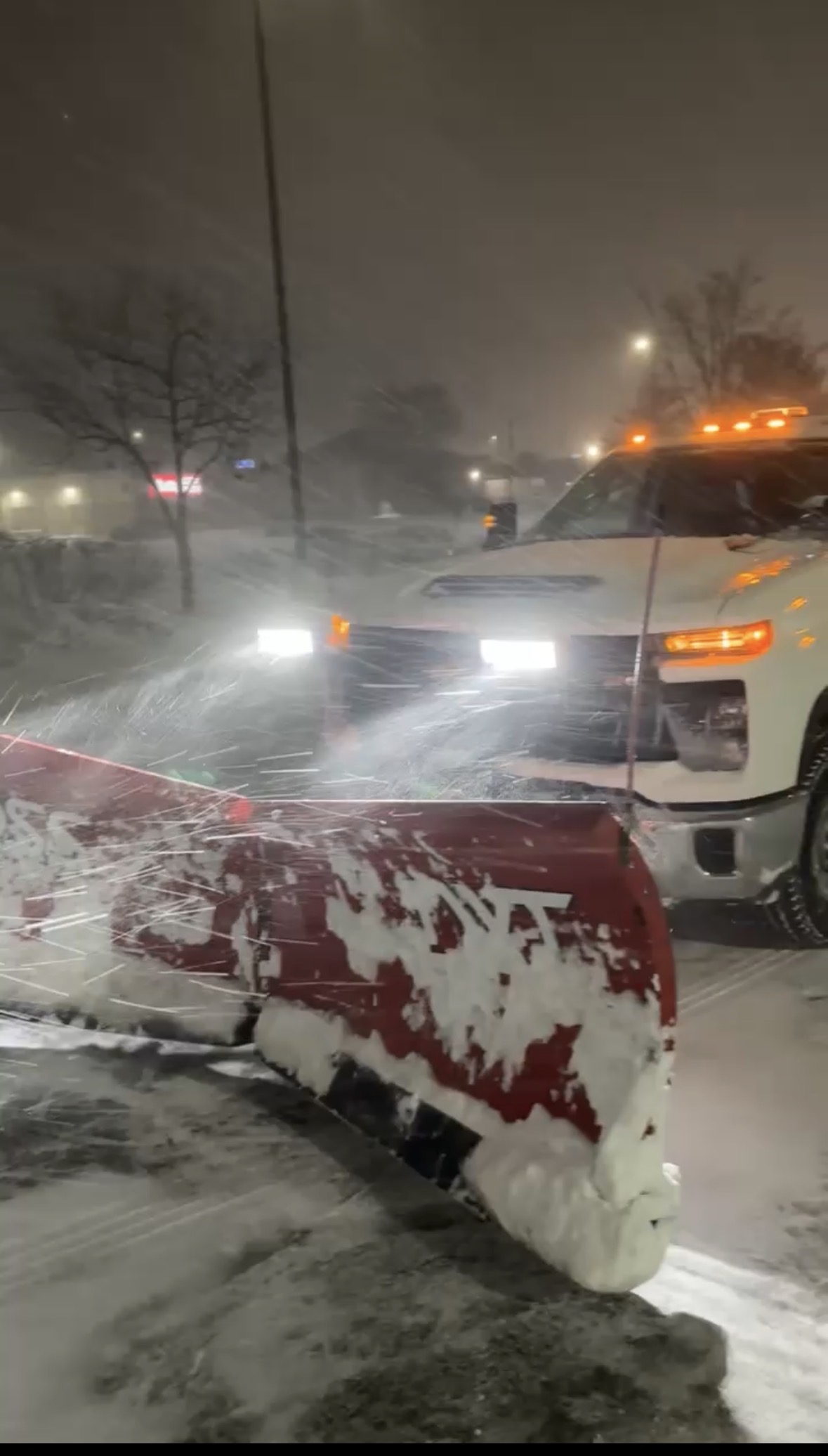 Swift plow truck pushing snow with a red plow blade during a snowstorm